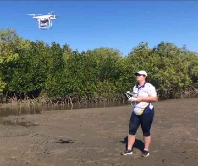 JCU PhD student Sophie Walker standing while operating a drone flying in front of her. 